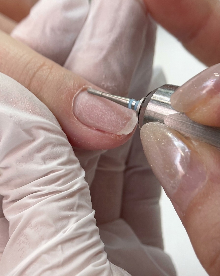 Ein kleiner, feinkörniger Fräser reinigt und glättet den Nagelfalz sowie den Nagelhautbereich eines Nagels.