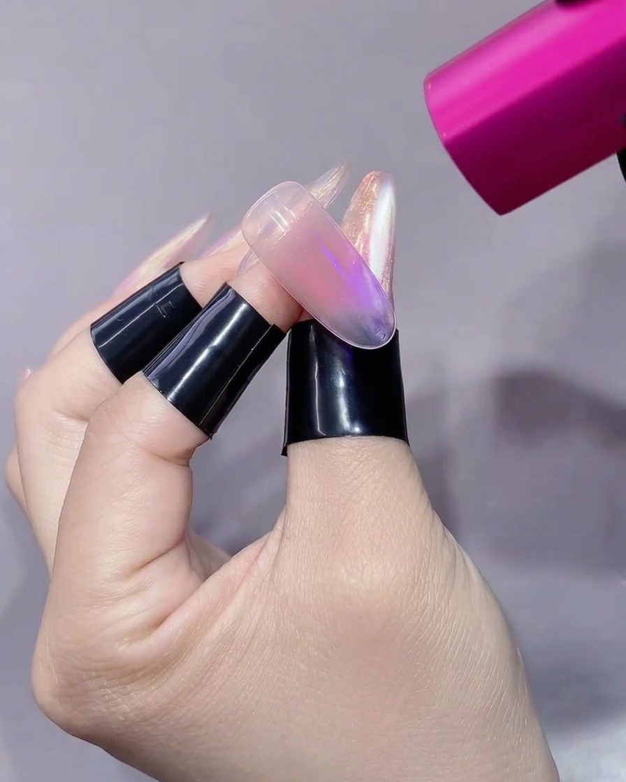 Eine pinke UV/LED-Handlampe zeigt direkt auf eine transluzente Nagelverlängerung auf einem Finger mit schwarzem Ständer.