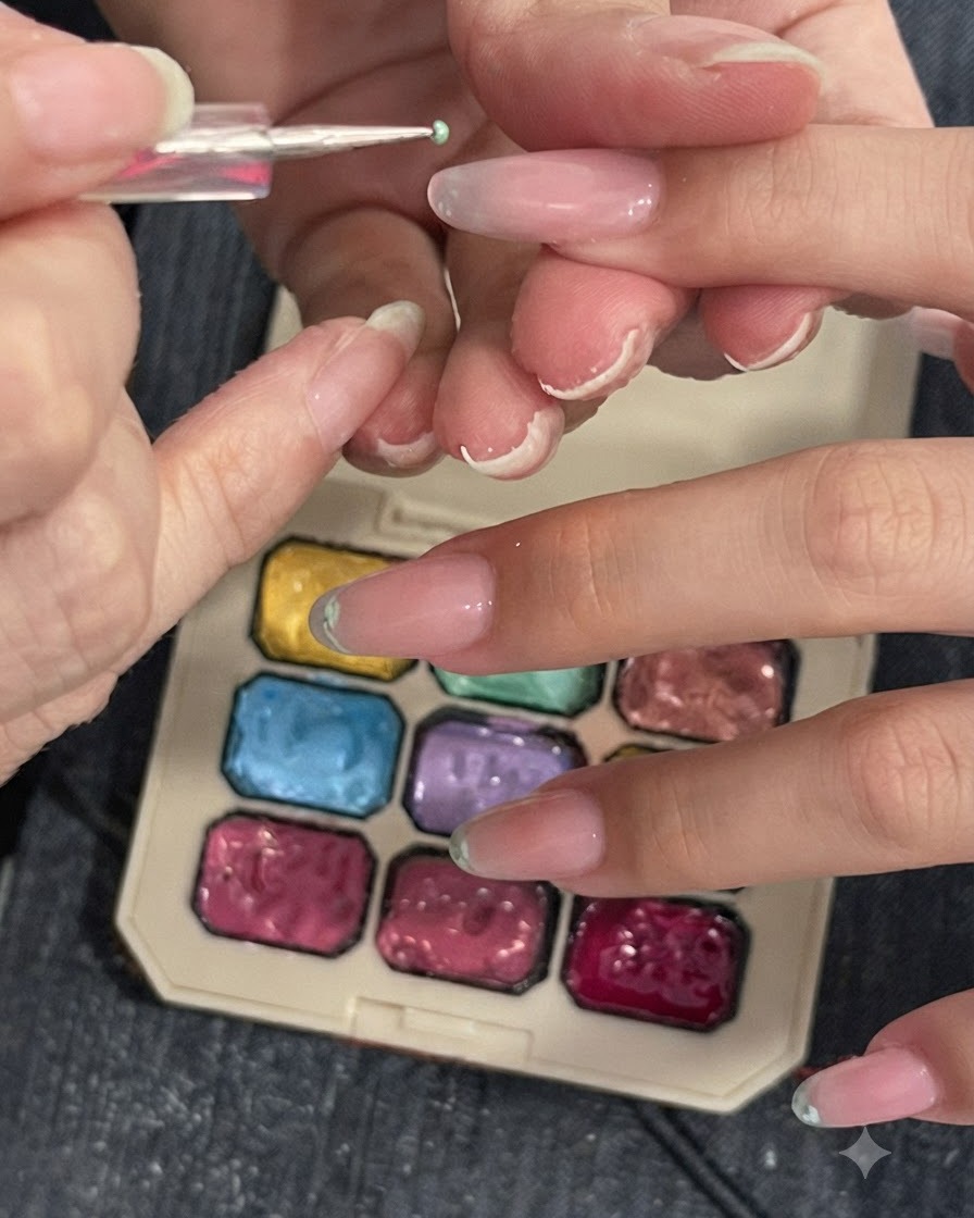 Ein Detailwerkzeug oder Schwämmchen tupft hellgrünes Pigment auf eine Nagelspitze neben einer Farbpalette.