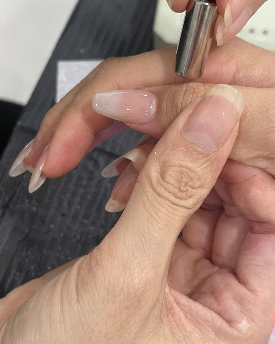 Ein kleiner Magnetstab wird nah an die Seite eines manikürten Nagels gehalten, um die Cat-Eye-Schimmerpartikel zu verschieben.