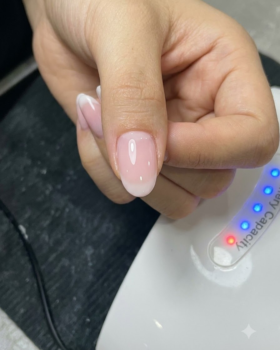 Ein Pinsel trägt eine Top-Coat-Schicht vor einer UV-Lampe auf einen manikürten Nagel auf.