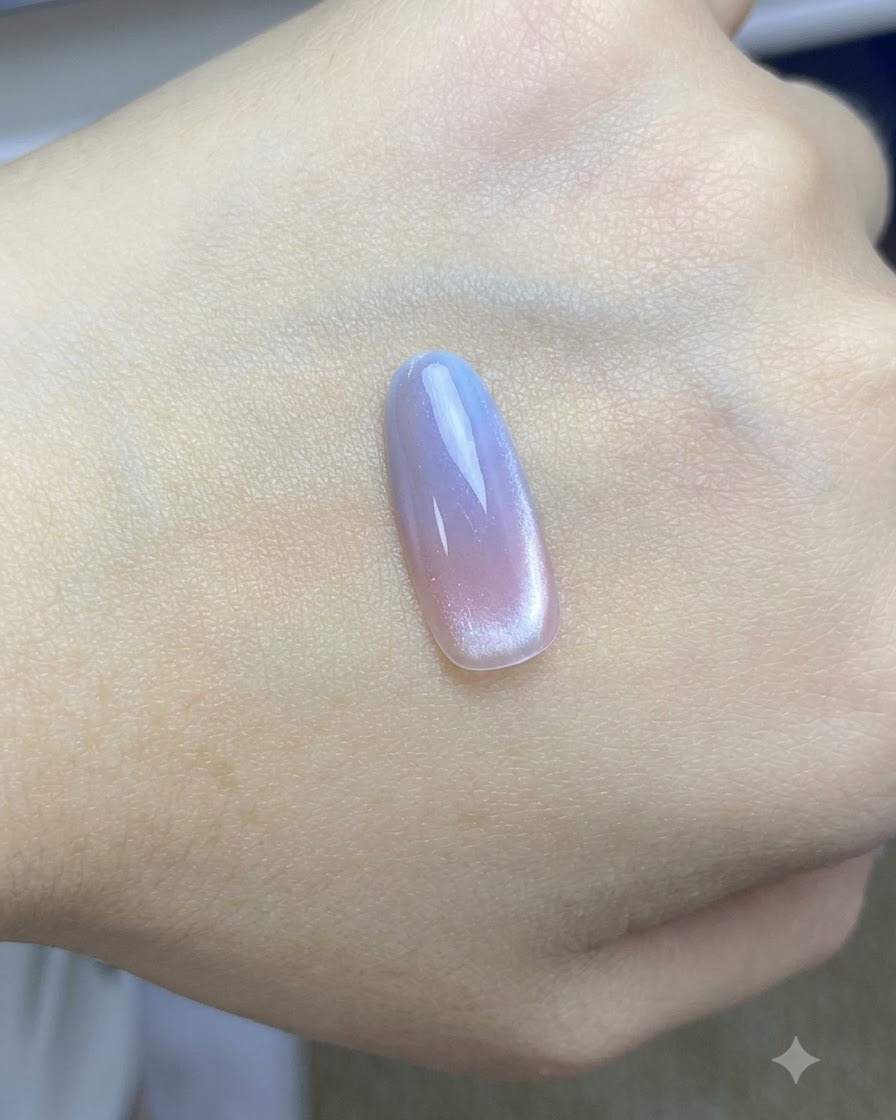 Ein Pinsel trägt einen finalen glänzenden Überzug über das fertige rosa-blaue Cat-Eye-Nageldesign auf.