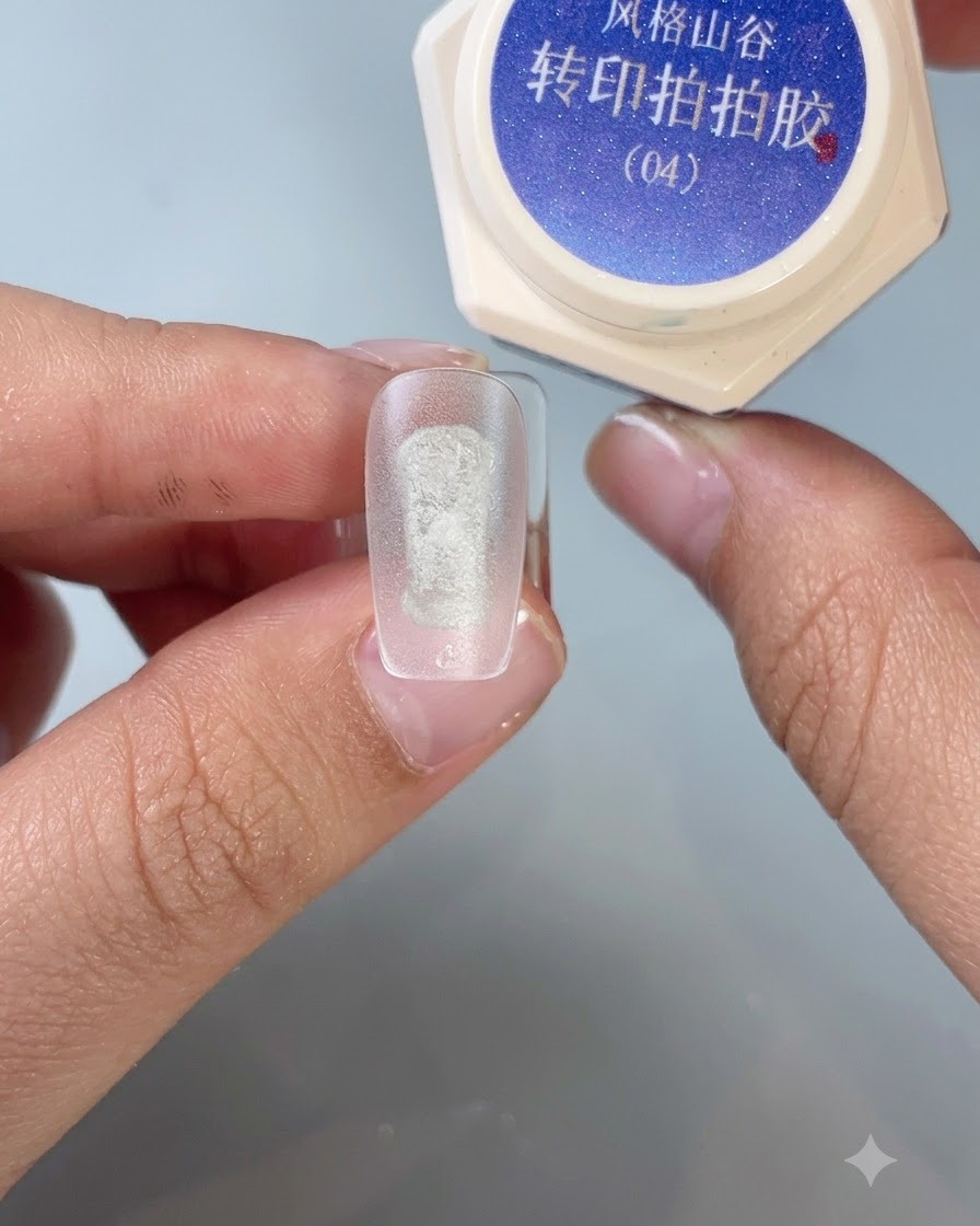 Ein Pinsel trägt Transfer-Stamping-Gel Nr. 4 auf die Mitte einer matten Übungsnagelspitze auf.