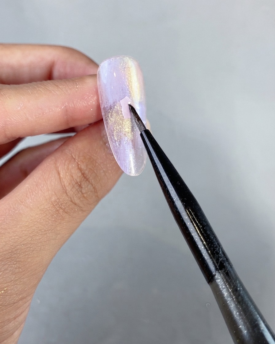 Ein feiner Linienpinsel platziert behutsam ein rosa Muschelstück auf einer nicht ausgehärteten lila Perlglanz-Gel-Nageloberfläche.