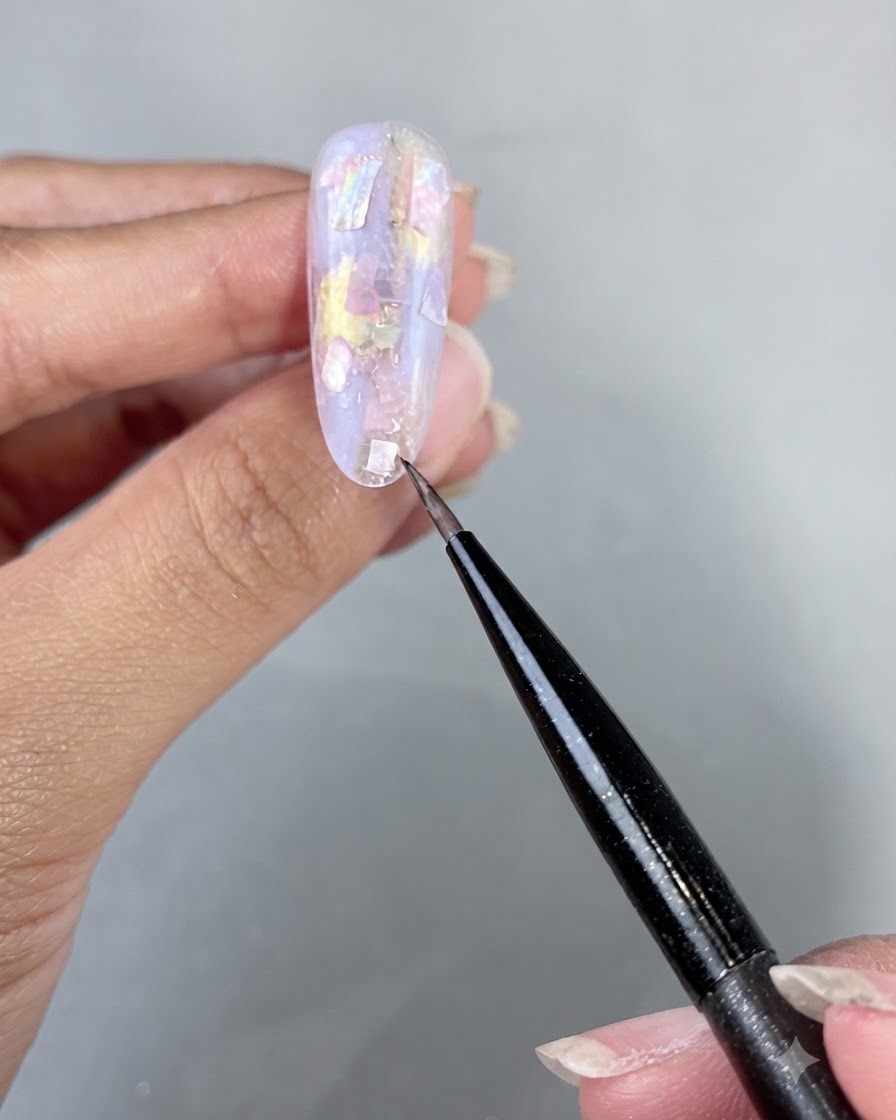 Eine Hand wird unter eine UV-/LED-Nagellampe gelegt, um die aufgetragenen Muschelstücke und das Builder Gel auszuhärten.