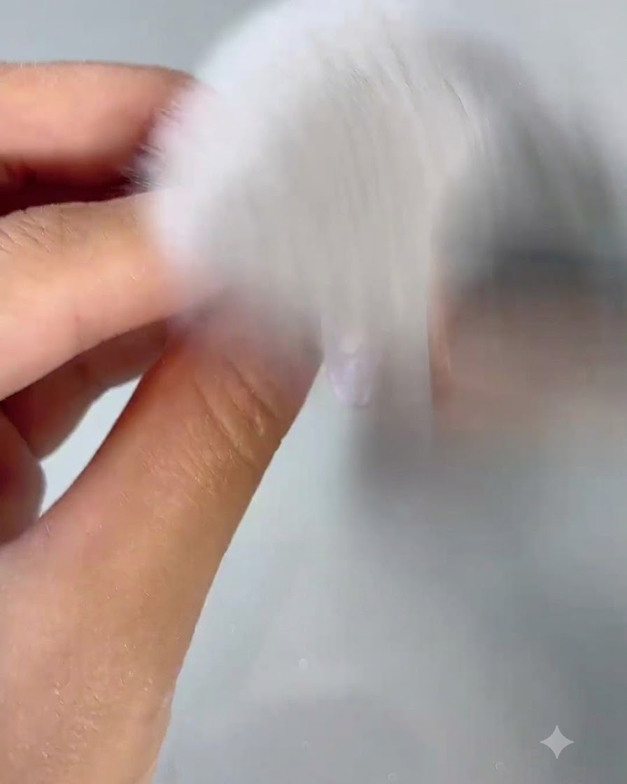 Ein flauschiger weißer Staubpinsel kehrt Nagelstaub von einem frisch gebufften Nagel ab.