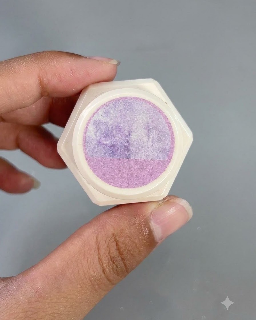 Ein sechseckiger weißer Behälter mit einem lila Aquarellmuster-Aufkleber auf dem Deckel, gehalten von Fingern.