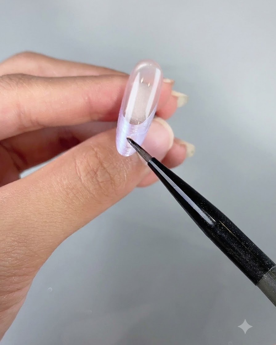 Ein feines Detailwerkzeug platziert kleine irisierende Muschelflocken entlang der French-Spitze eines Nagels.