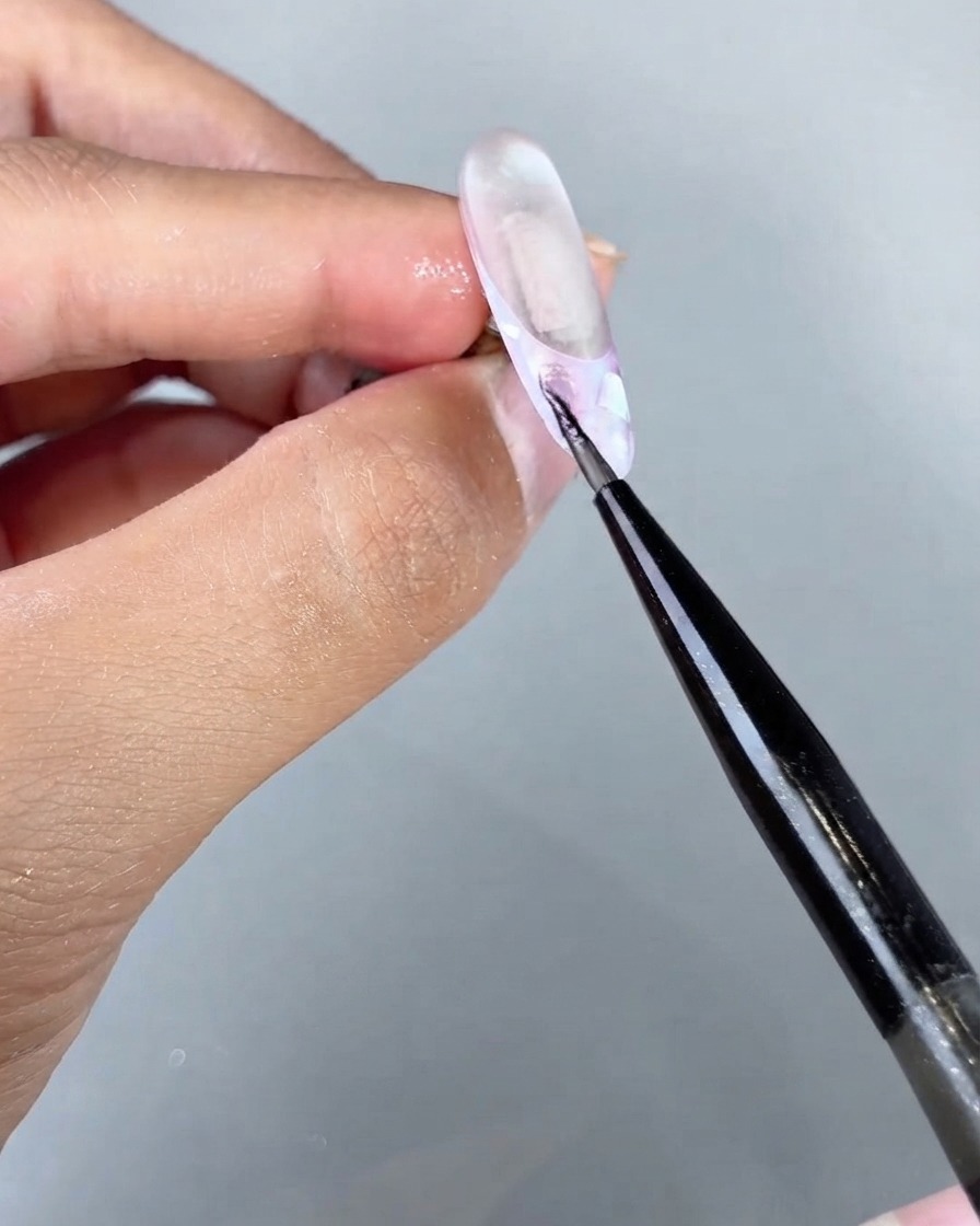 Ein feiner Pinsel trägt magisches Sea Cat Eye Gel auf einen spezifischen Bereich eines strukturierten Nageldesigns auf.
