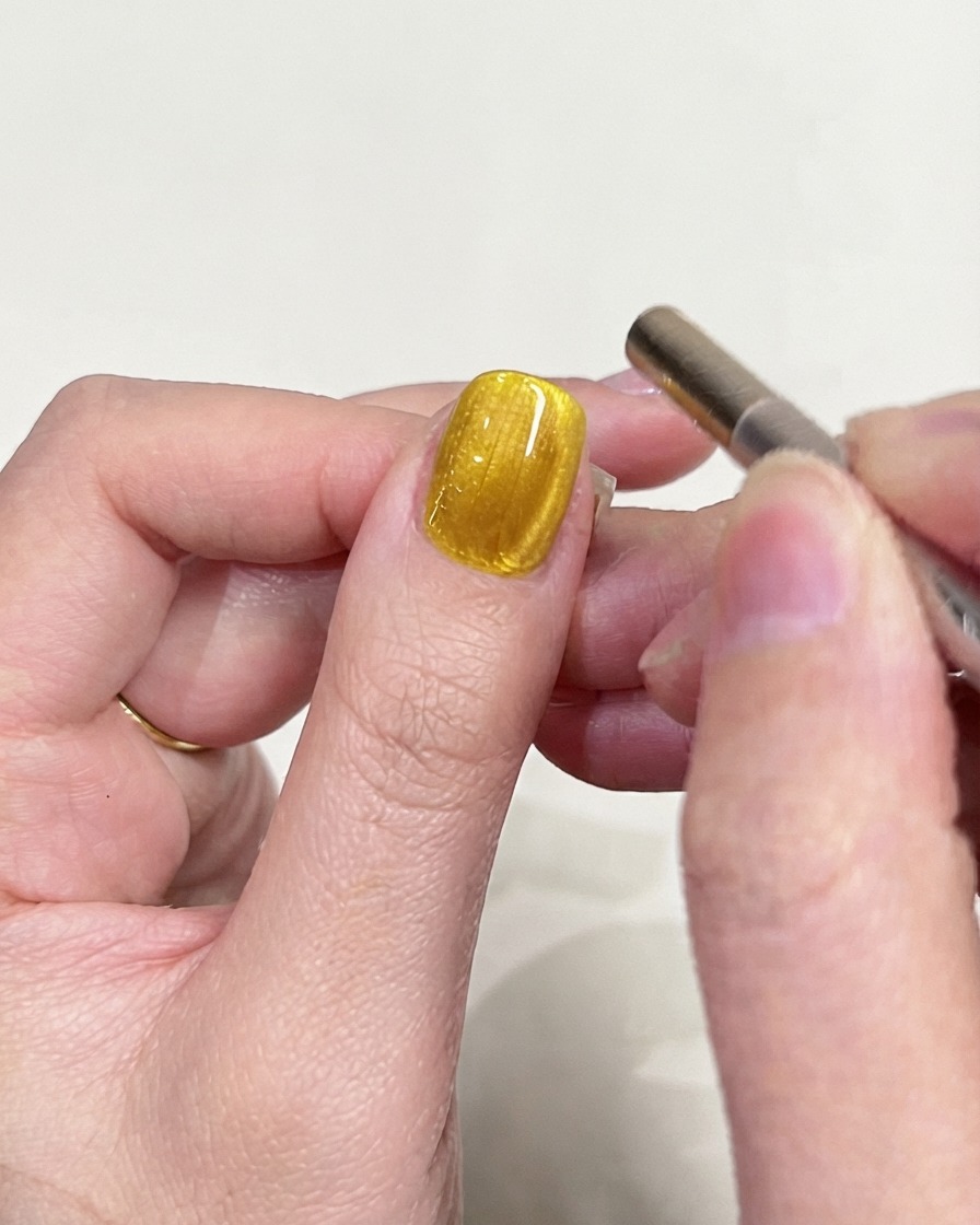 Ein detailliertes Inspektionsfoto eines gelben Cat-Eye-Gel-Nagels mit Fokus auf die magnetische Lichtreflexion.