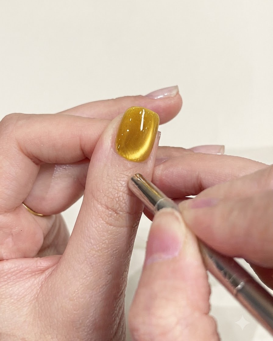 Ein Präzisionsmagnet-Stiftwerkzeug, das zum Verfeinern des Schimmerpfads auf einem gelben Cat-Eye-Nagel verwendet wird.