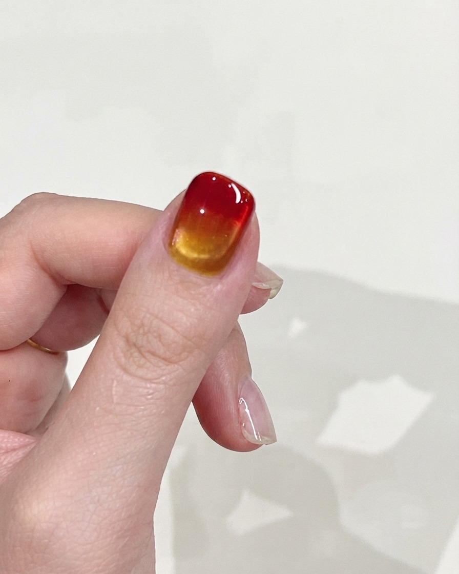 Eine Hand wird vor einem schlichten Hintergrund gehalten und zeigt die glatte Farbverlaufstextur sowie das glänzende Finish des Nagels.