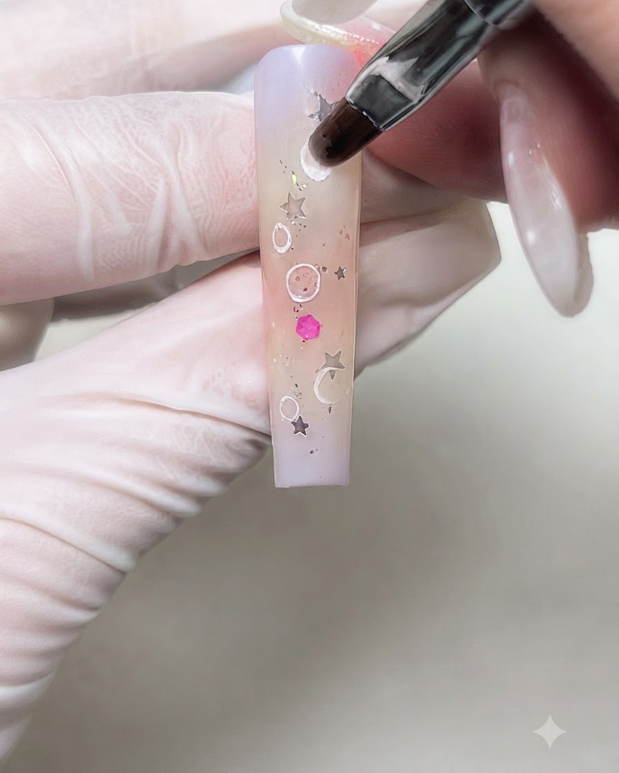 Ein Nail-Art-Pinsel verblendet weich die inneren Ränder von weißen Creme-Kreisen auf einem Gradienten-Nagel.