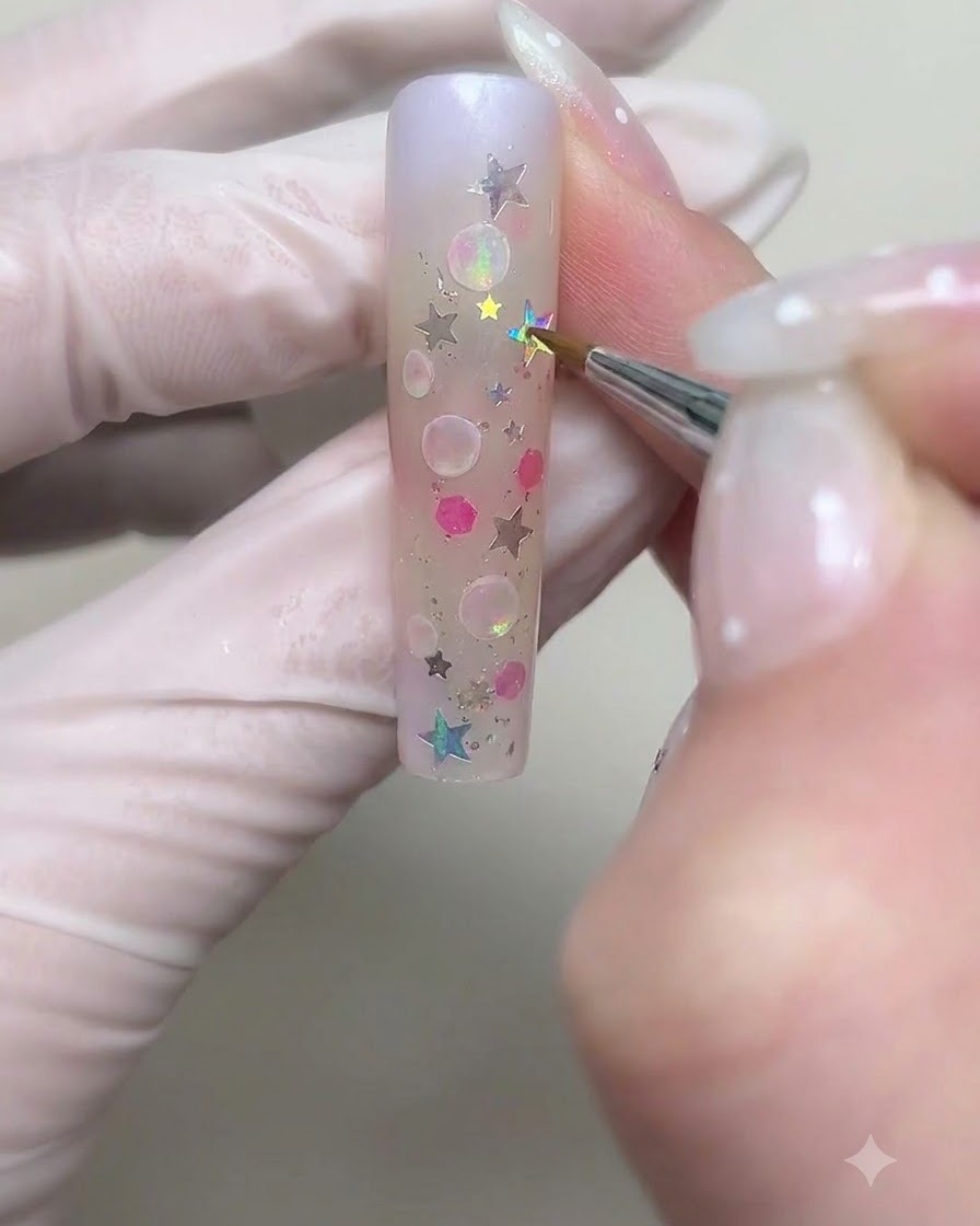 Ein feiner Pinsel zeichnet größere kreisförmige Blasen-Umrisse mit weißem Cremegel auf den Nagel.