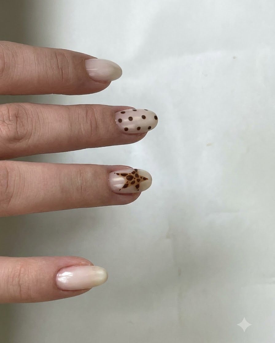 Ein Pinsel trägt klaren Überlack über einen Nagel mit braunen Polka Dots und einem Stern-Design auf.