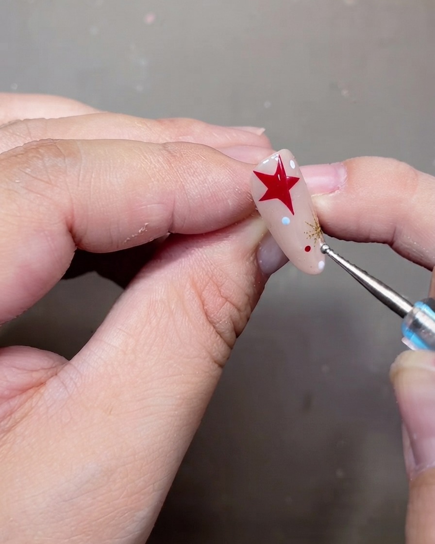 Ein Dotting-Tool platziert winzige weiße und rote Polka-Dots auf einem verzierten Nude-Gel-Nagel.