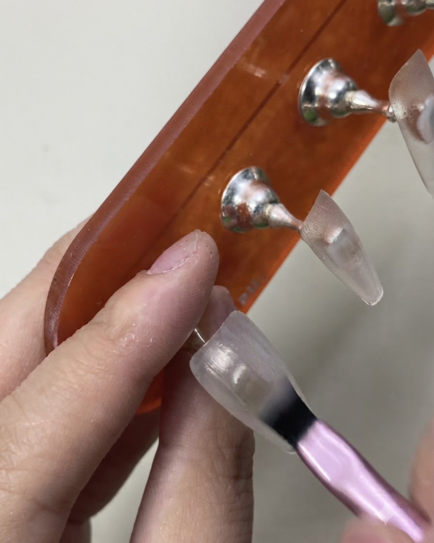 Ein Pinsel trägt sorgfältig den ersten Anstrich von sheerem, milchig-weißem Gel-Polish auf einen Nagel-Praxistip auf.