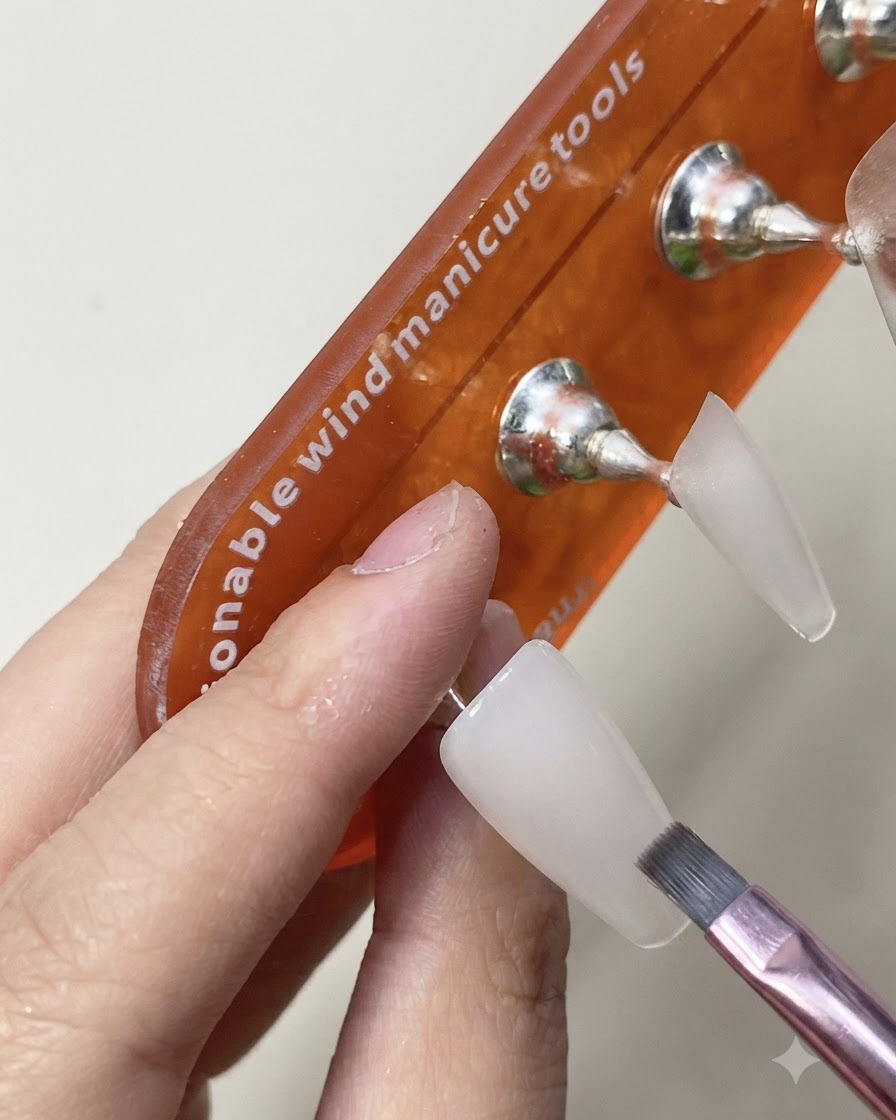 Ein Pinsel trägt eine glänzende Top-Coat-Schicht auf die ausgehärtete, milchig-weiße Nagellverlängerung auf.