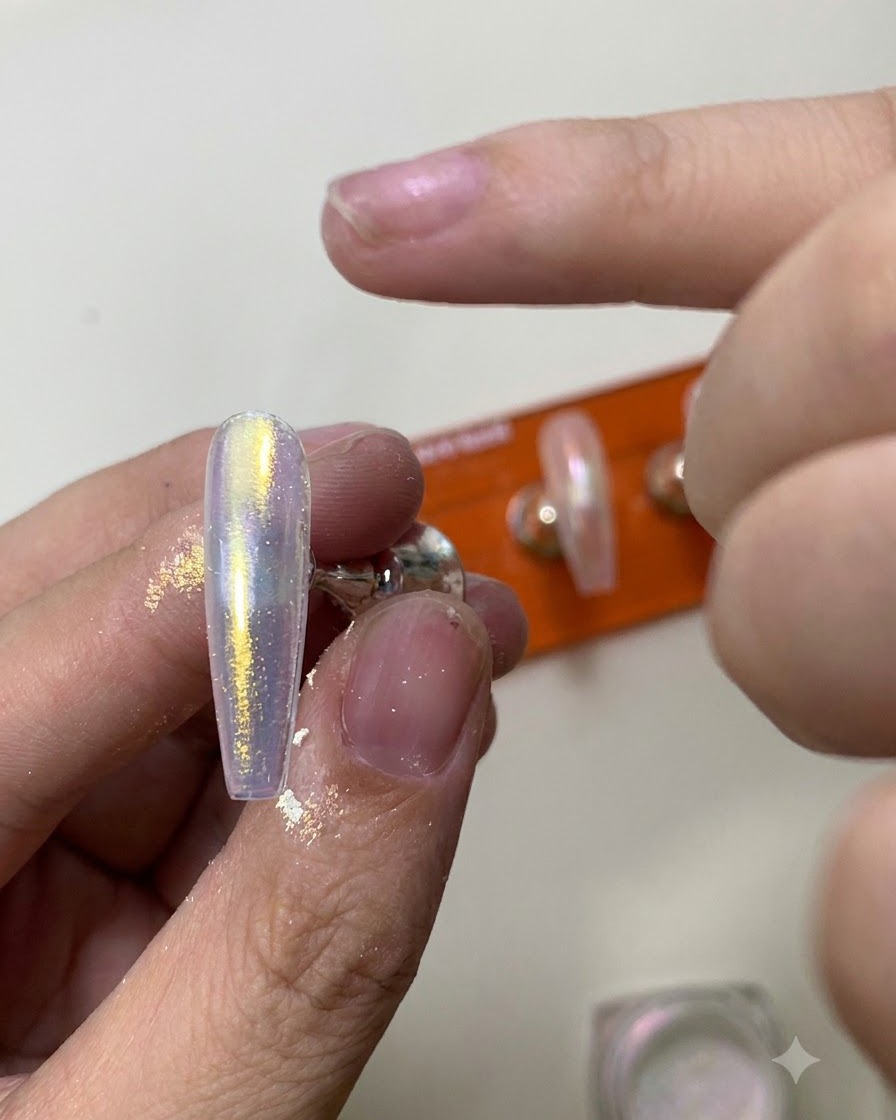 Ein Silikon-Applikator-Tool reibt schimmerndes Aurora-Chrome-Puder auf eine glänzende Nageloberfläche.