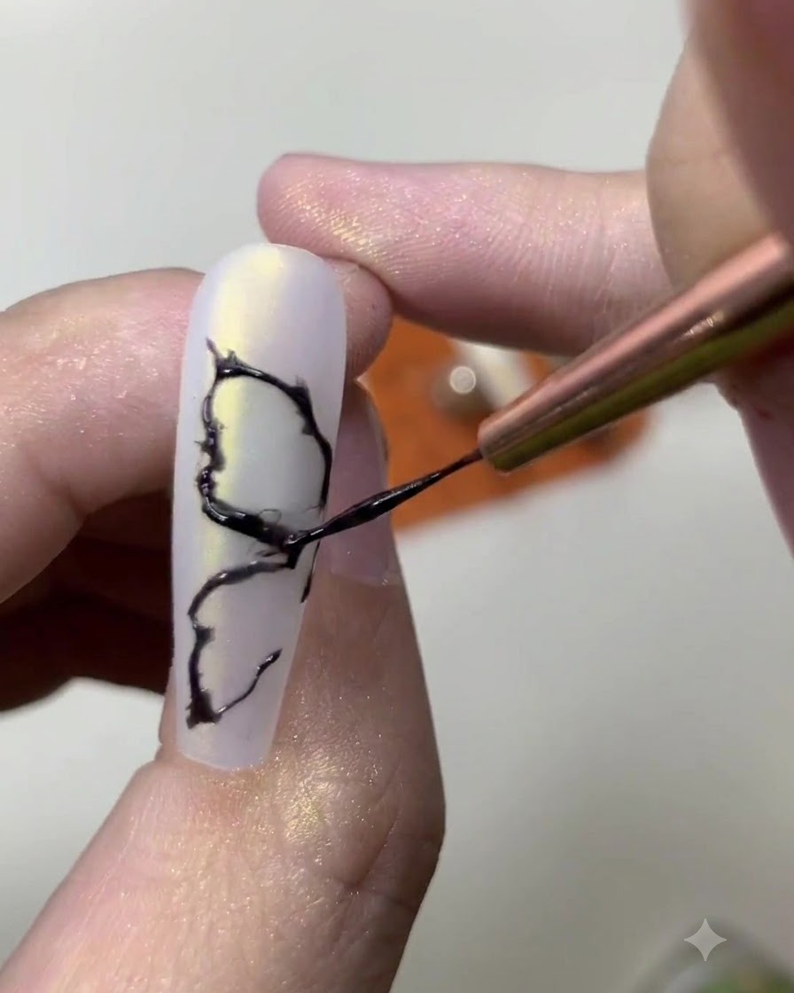 Nahaufnahme einer Nageldesignerin, die feine innere Details zu einem gemalten schwarzen Schmetterlingsflügel-Design hinzufügt.