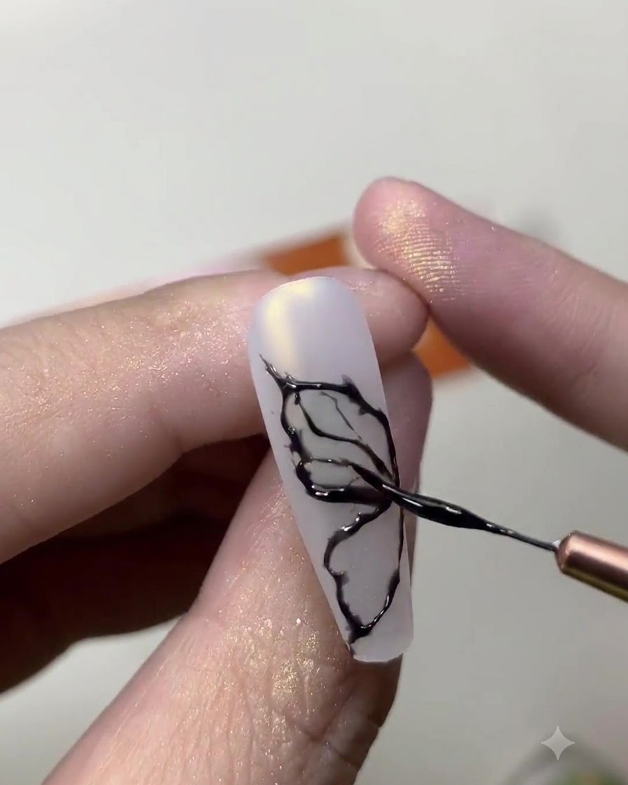 Eine Nahaufnahme einer Nageldesignerin, die mit einem feinen Pinsel filigrane schwarze Schmetterlingsflügel-Linien auf einen milchig-weißen Nagel zeichnet.