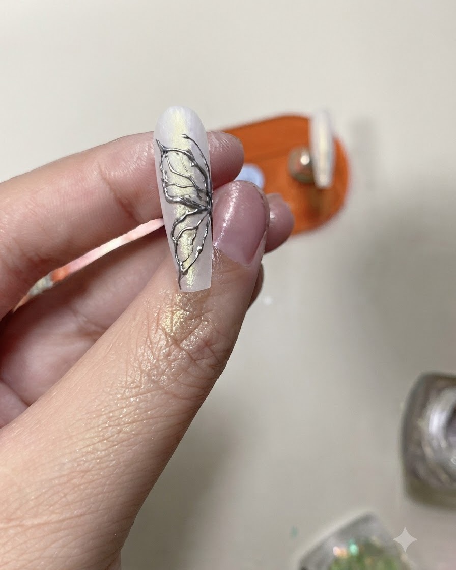 Ein Top-Coat-Pinsel trägt eine klare Schutzschicht über ein fertiges Silver-Chrome-Schmetterlings-Nageldesign auf.