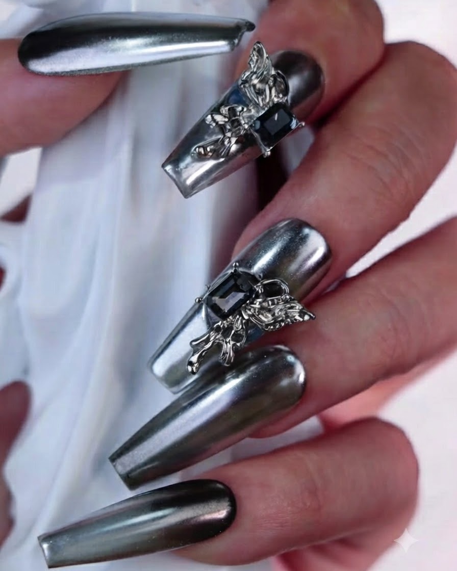 Makroansicht eines künstlichen Silbergold-Nagels mit einer detailreichen 3D-Schmetterlingsverzierung und einem dunklen, rechteckigen Edelstein.