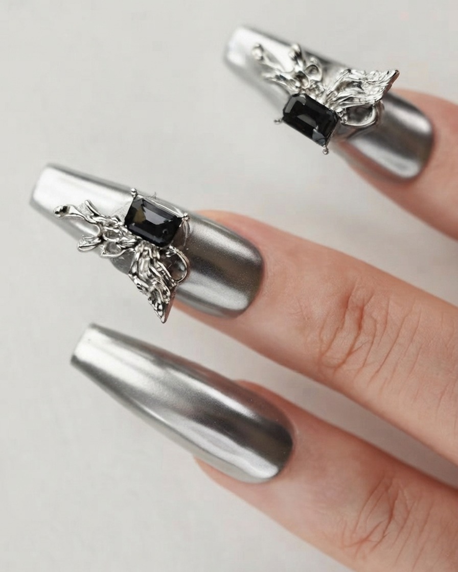 Nahaufnahme eines Fingers mit einem silbernen Chromnagel, der mit einem detaillierten 3D-Schmetterlingscharm und dunklen Kristallen verziert ist.