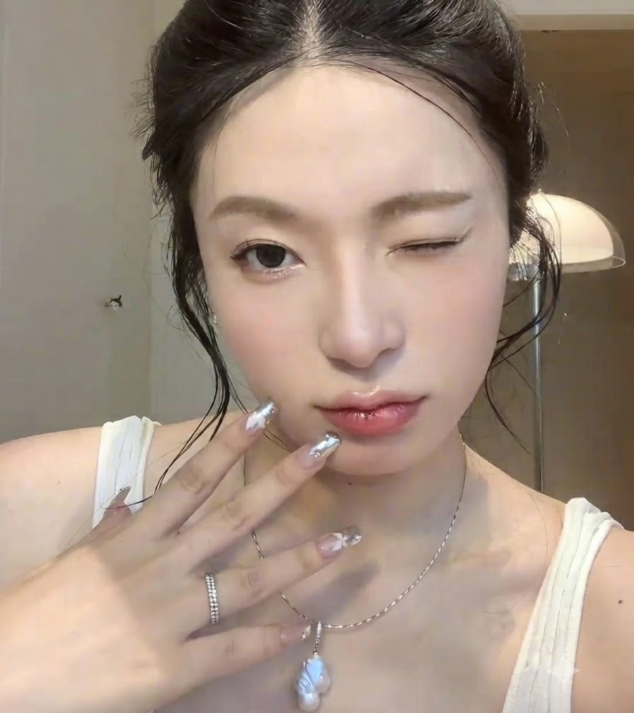 Nahaufnahme einer Hand mit Silber-Chrome-Nail-Art, die mit einem zwinkernden Gesichtsausdruck nahe ans Gesicht gehalten wird.