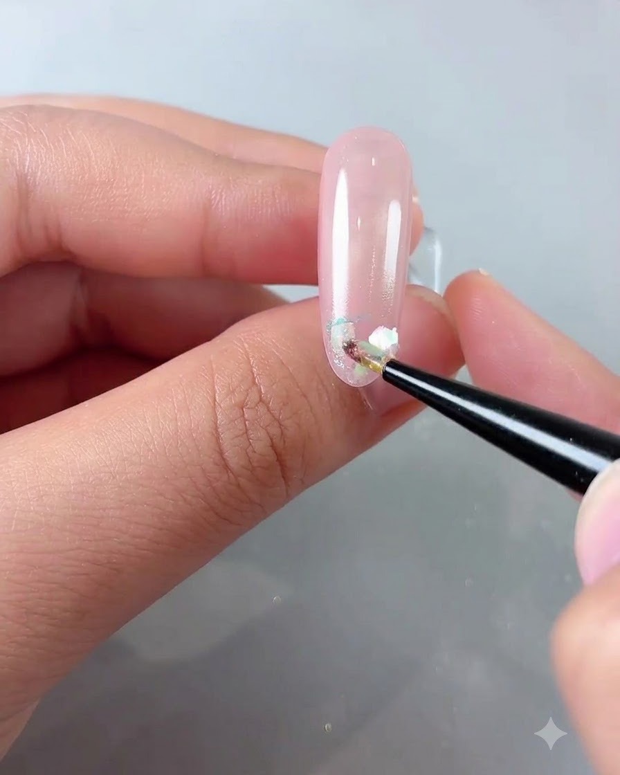 Ein feiner Pinsel platziert schimmernde Cloud-Powder-Flocken auf der Vorderkante eines rosafarbenen Nagels.