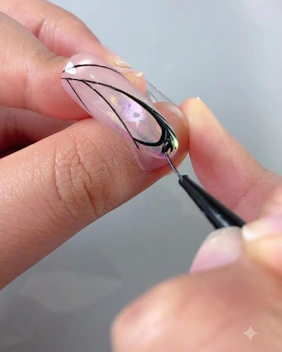 Eine Nahaufnahme einer Hand, die einen Liner-Pinsel mit schwarzem Gel verwendet, um Details in einem Schmetterlingsflügeldesign auf einem Nagel auszufüllen.