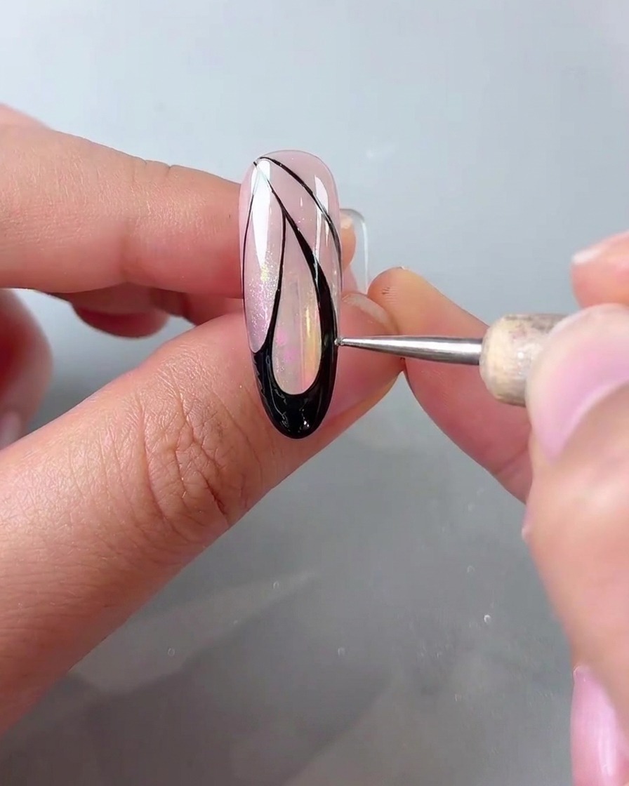 Ein Dotting-Pen setzt kleine weiße Punkte entlang des äußeren Rands einer schwarzen Schmetterlingsflügel-Nagelkunst.