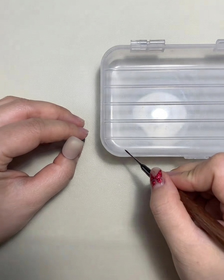 Eine Nail-Artist hält einen feinen Liner-Pinsel in die Nähe einer Übungsnagelspitze.