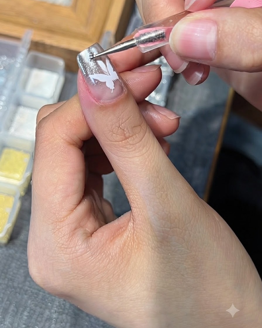 Ein Dotting-Tool platziert einen kleinen Strassstein auf einem Nagel mit einem weißen Schmetterlingsdesign.
