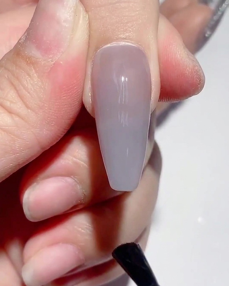 Ein Pinsel trägt matten Top Coat auf die Oberfläche eines lackierten Nagels auf.