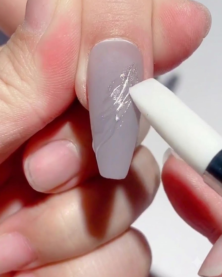 Ein Silikon-Stiftwerkzeug reibt silbernes Spiegelpuder auf ausgehärtete Gel-Linien auf einem taupefarbenen Nagel.