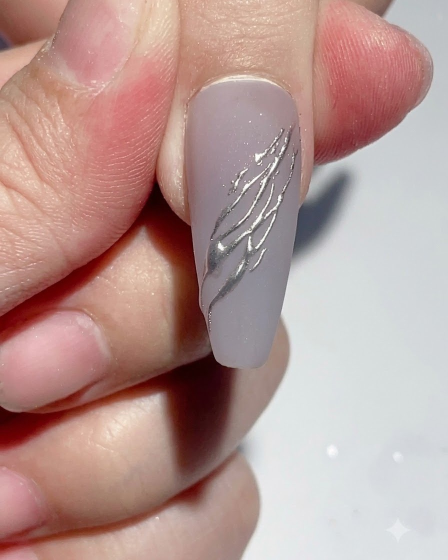 Ein Liner-Pinsel trägt einen kleinen Punkt klaren Strassklebers auf einen verzierten Nagel auf.