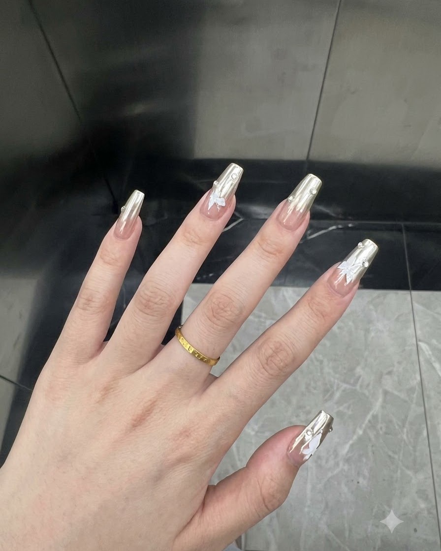 Nahaufnahme eines Daumennagels mit silbernem Chrom-Lack und einem kleinen weißen Schmetterlings-Sticker.