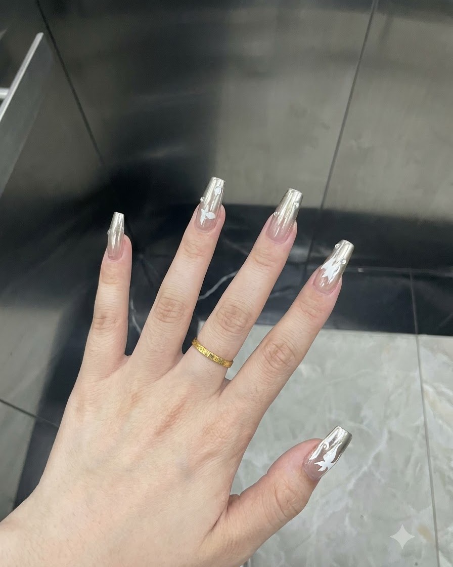 Detaillierte Nahaufnahme eines Fingers mit einem weißen Schmetterlings-Aufkleber auf einem silbernen Chrom-Nagel.
