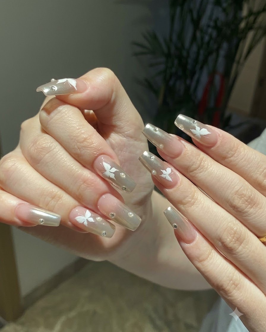 Zwei Hände nebeneinander posiert und präsentieren die vollständige silberne Chrom- und Schmetterlings-Nagelkunst unter warmem Raumlicht.