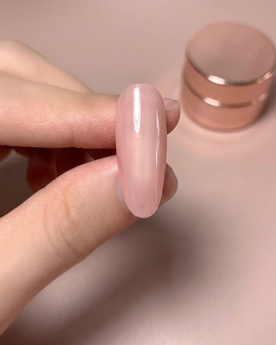 Ein Finger, der den Nagel nach dem Auftragen einer zweiten Schicht glänzenden Nude-Farbgels zeigt.