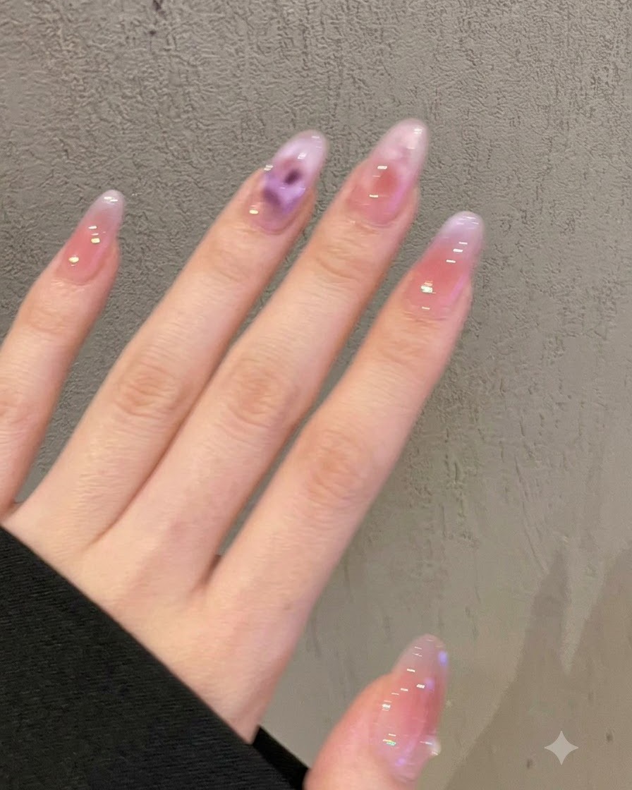 Nahaufnahme von Nägeln mit einem sanften violett-pinken, milchigen Ombré-Verlauf und miniaturen Kristallverzierungen.