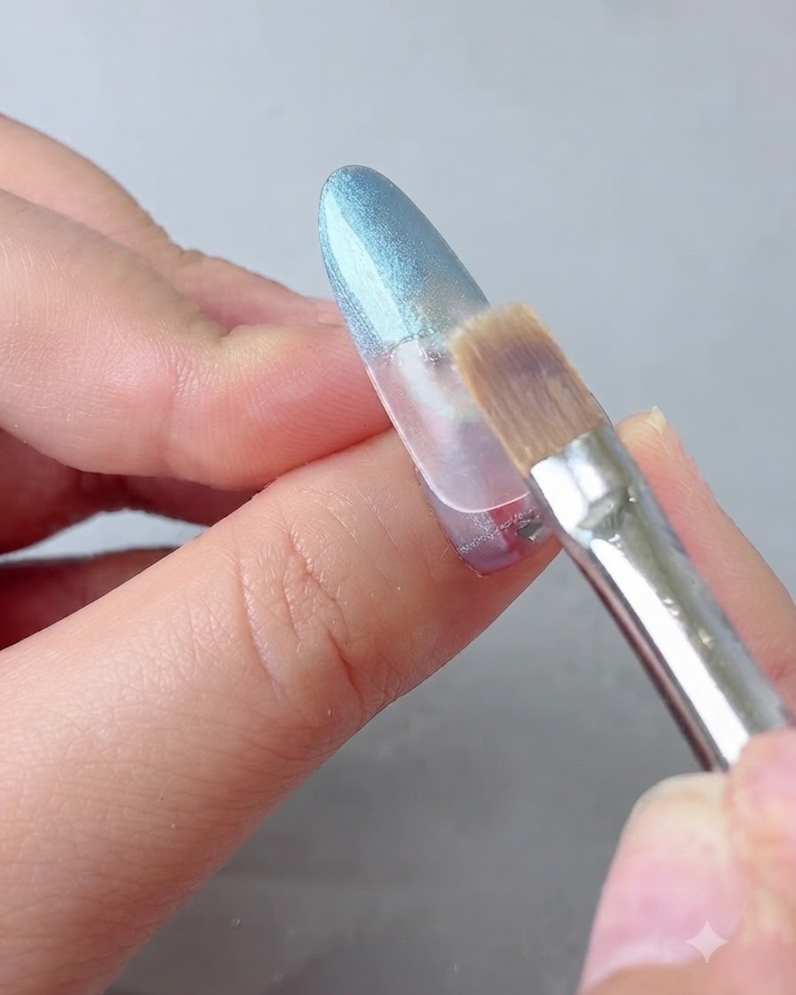 Ein Verblendungspinsel streicht den Übergang des blauen Gels auf einem Nagel weich aus.