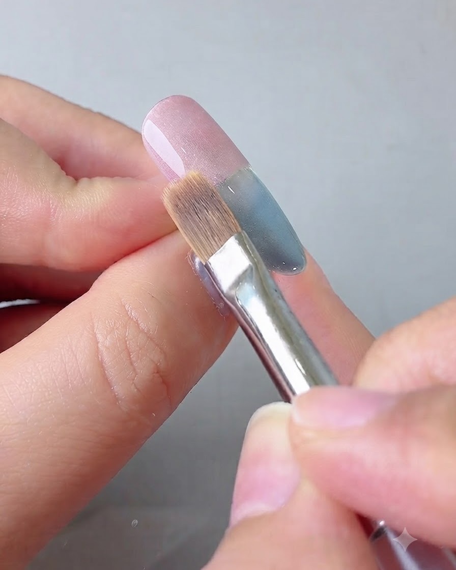 Ein Verblendungspinsel zieht das rosa Gel sanft zur Nagelmitte hin aus.