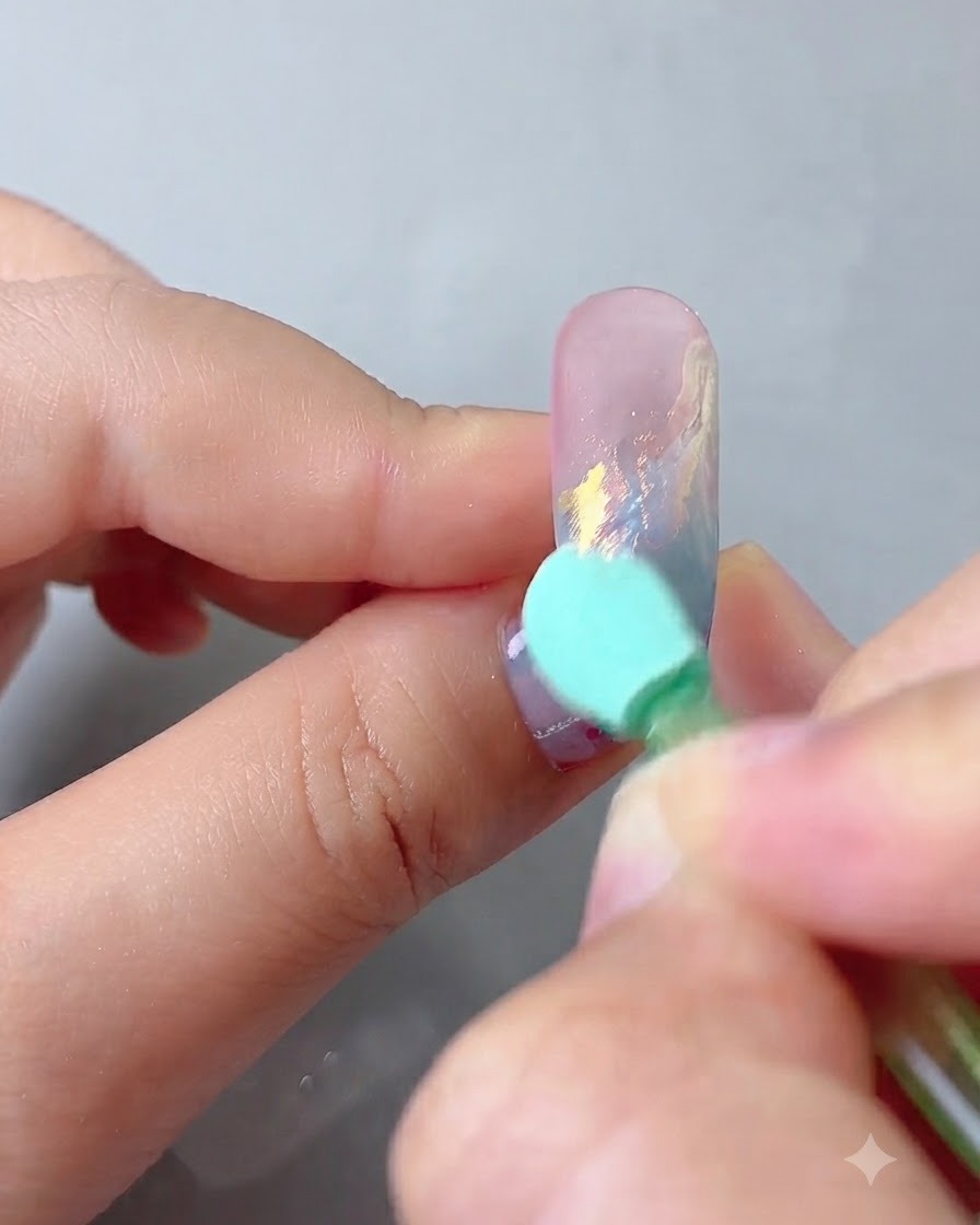 Ein Applikatorschwamm reibt Aurora Magic Mirror Powder auf die dekorierte Nageloberfläche ein.