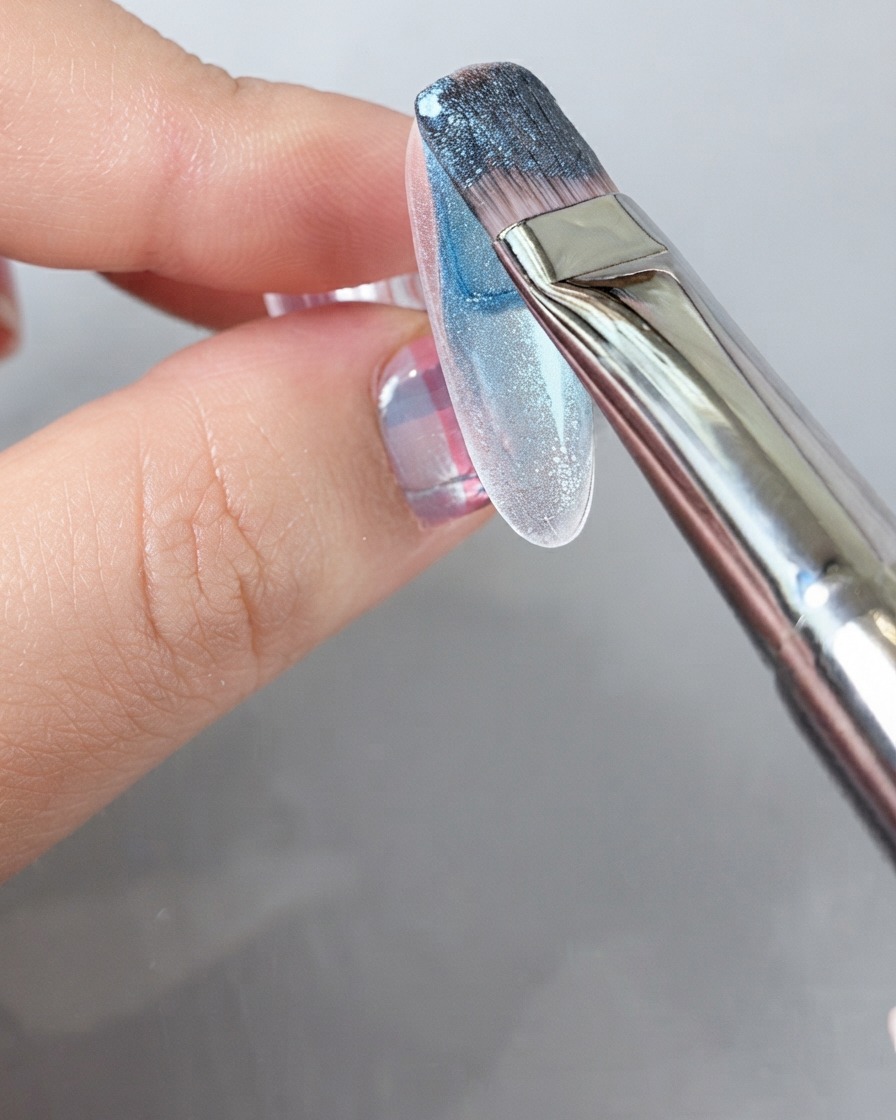 Ein Pinsel trägt einen satten blauen Gelack über die gesamte Oberfläche eines Nagels auf.