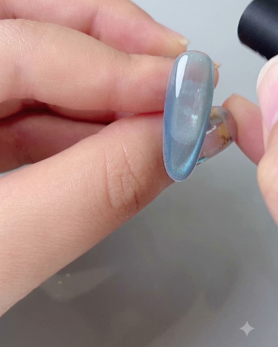 Ein Magnetwerkzeug formt den seitlichen Reflektionsbogen auf einem blauen Cat-Eye-Gel-Nagel.