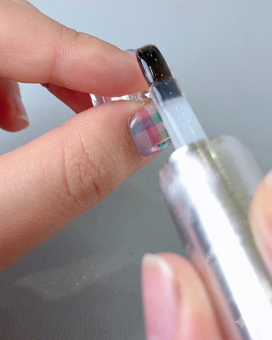Ein Pinsel trägt einen klaren, glänzenden Top Coat auf die Oberfläche eines fertigen mustergültigen Nagels auf.