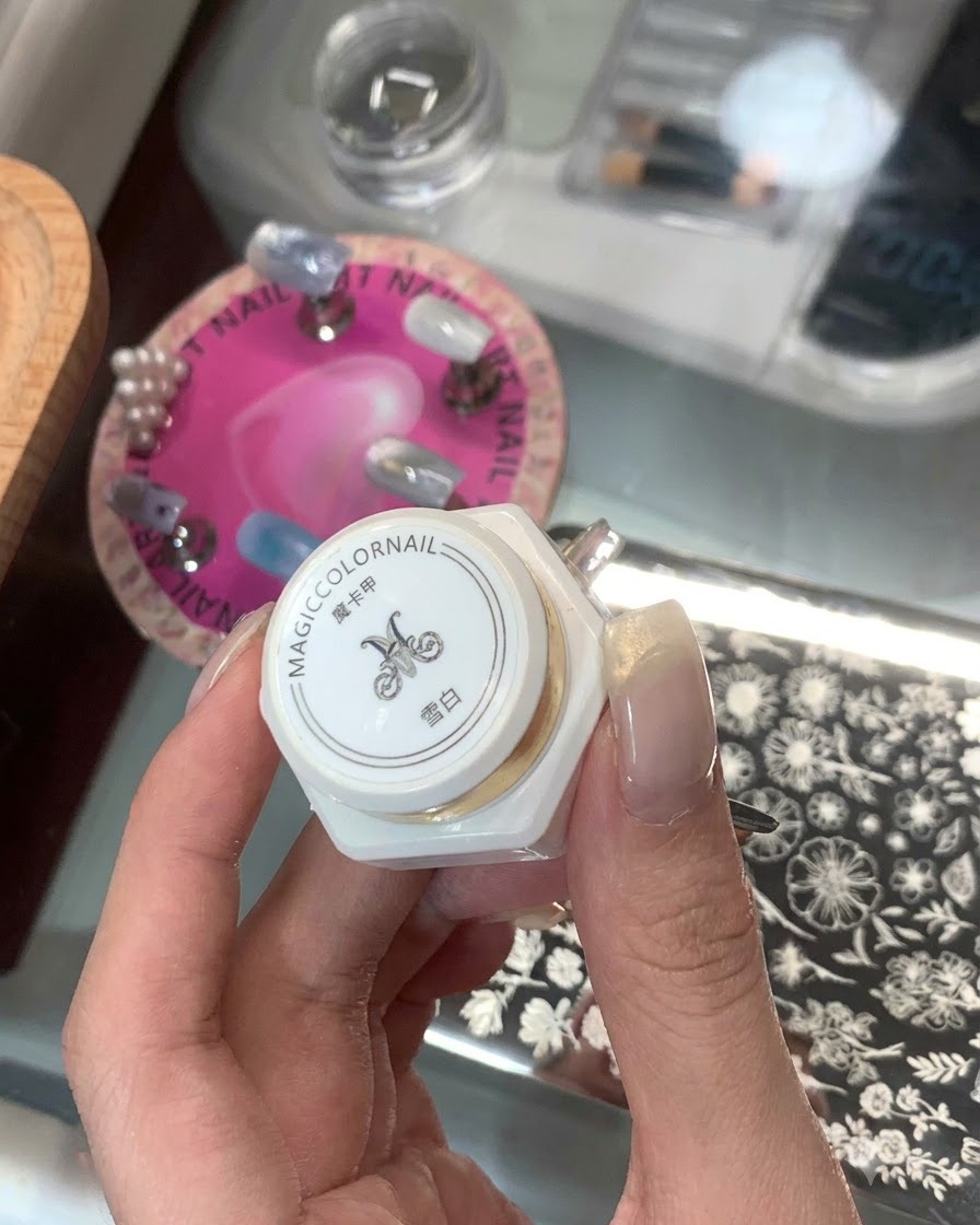 Eine Hand hält ein weißes Stamping-Produkt in einer Flasche mit asiatischen Schriftzeichen, im Hintergrund ist eine Nagel-Stamping-Platte zu sehen.