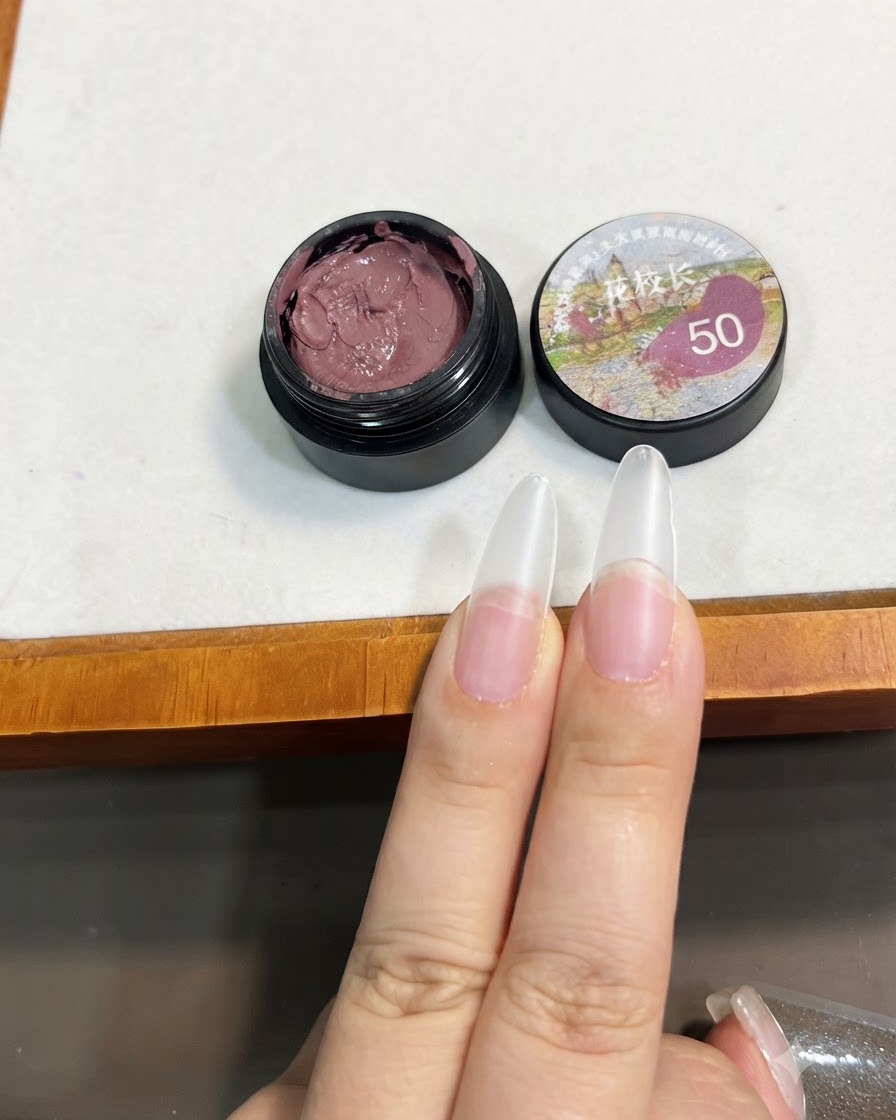Ein Pinsel hält eine kleine Menge Bohnenpasten-rosa Solid Gel nahe der Spitze einer klaren Nagelverlängerung.